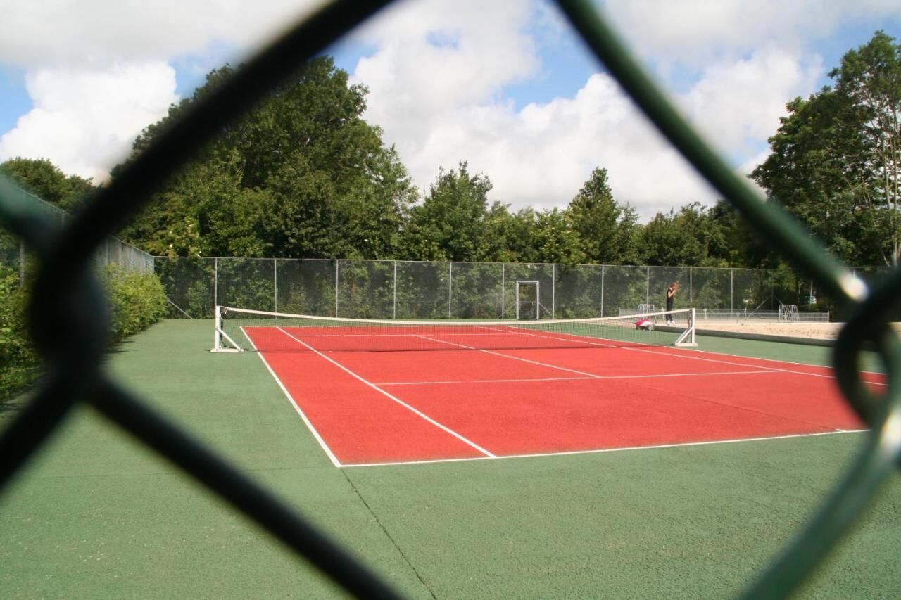 Un court de tennis avec un filet, entouré d’une clôture et d’arbres.