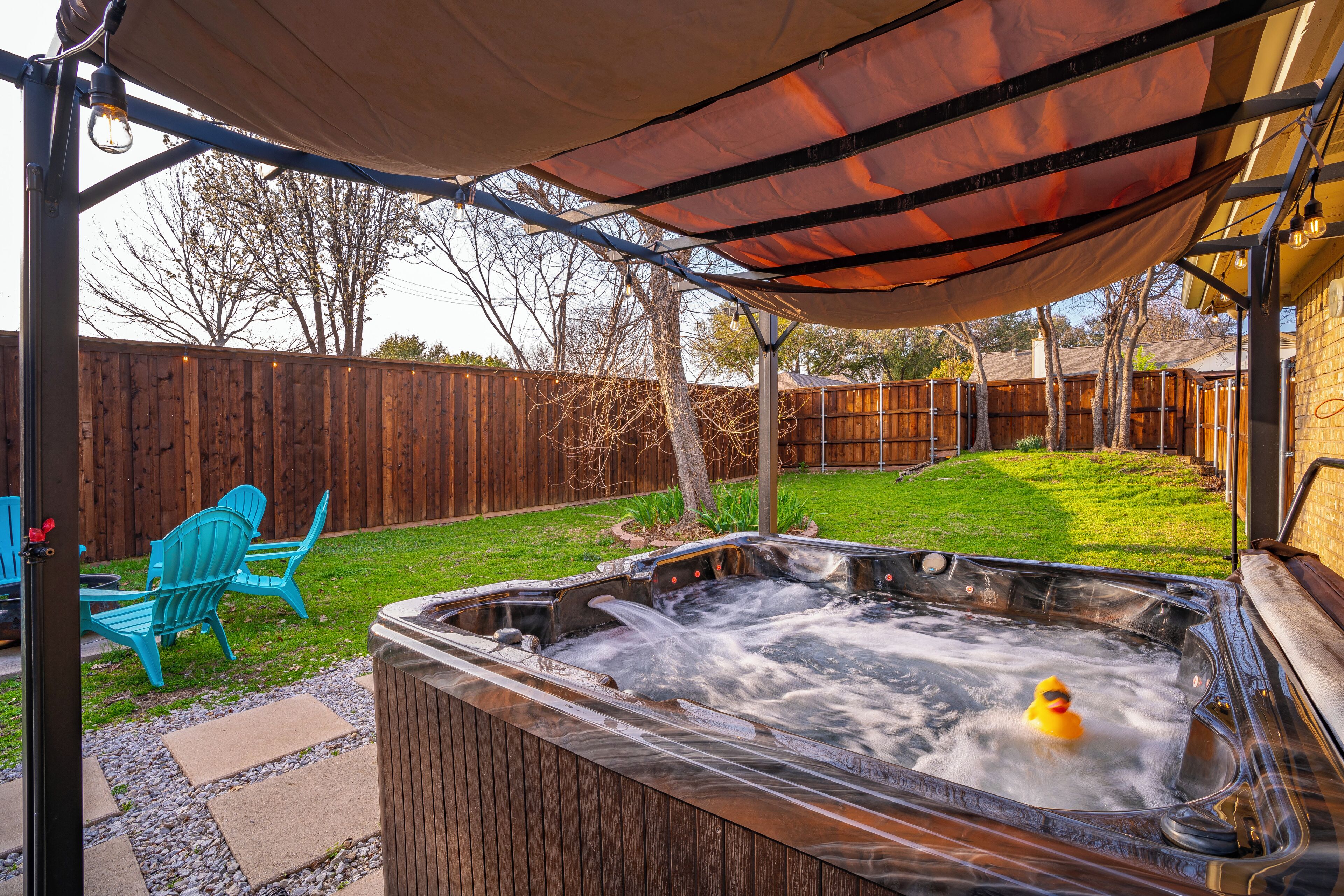 Un bain à remous installé sous une tonnelle, avec une terrasse en bois, des chaises et une pelouse.