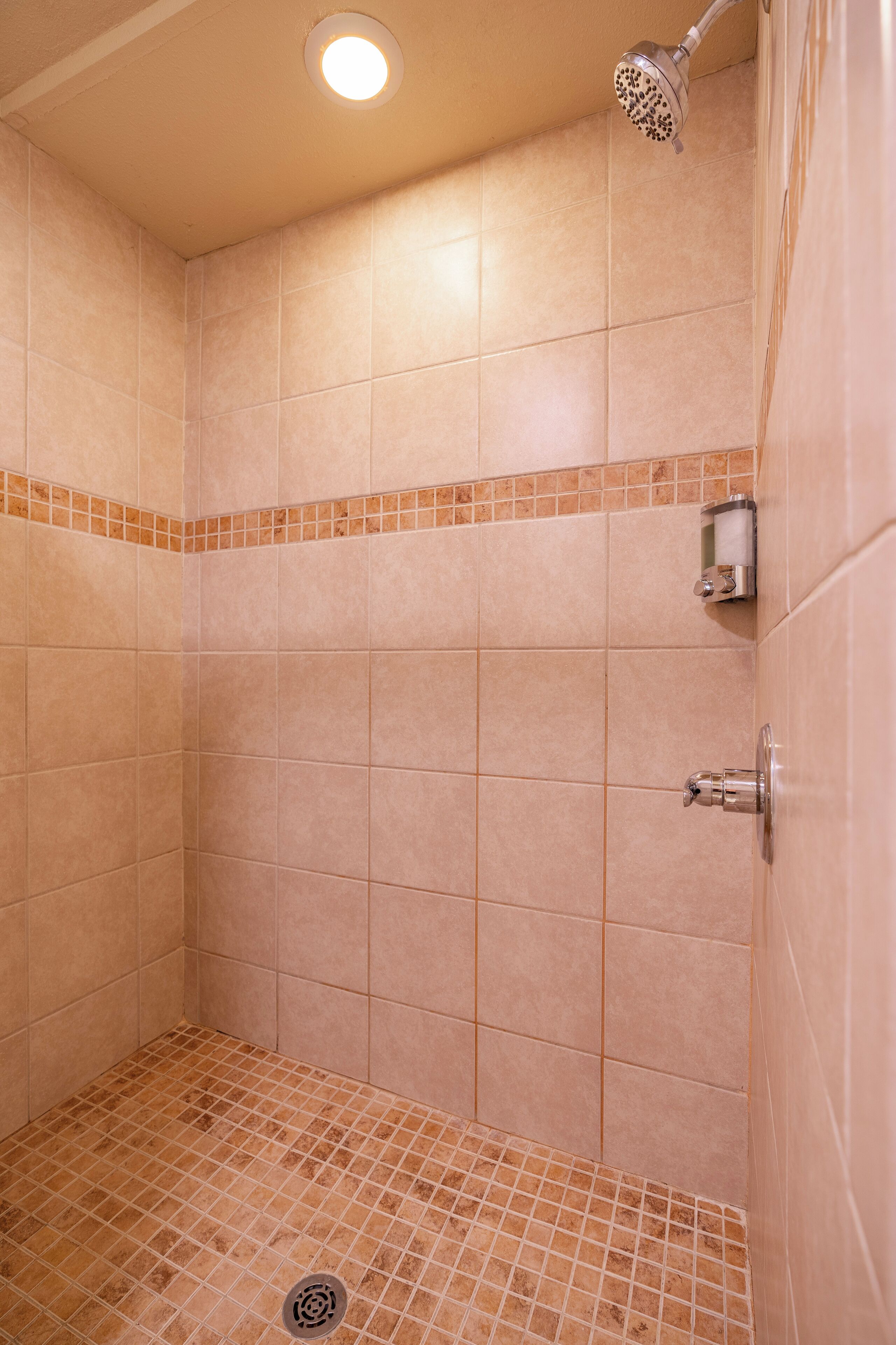 Ducha con azulejos color beige, un cabezal de ducha y un desagüe.