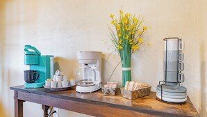 Een keukenblad met een koffiezetapparaat, een waterkoker, een vaas met gele bloemen en een stapel borden.