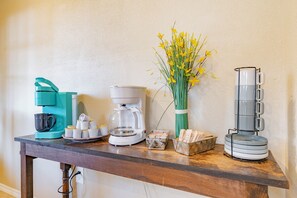 A kitchen counter with a coffee maker, a tea kettle, a vase with yellow flowers, and a stack of plates.