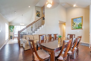 A spacious dining area with a wooden table and chairs, a staircase, and a painting on the wall.