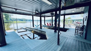 Terraza techada al aire libre con vista a un lago, bancos de madera y una hamaca.