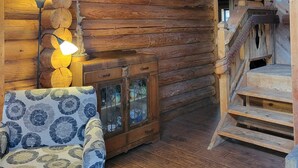 Interior d'una cabana de fusta amb una escala de fusta, un sofà amb tapisseria estampada i un armari de fusta amb portes de vidre.