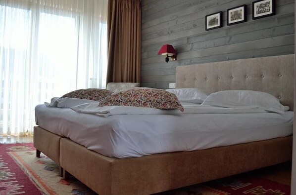 Una cama doble con almohadas estampadas con motivos florales, una lámpara de pared roja y un cabecero gris.