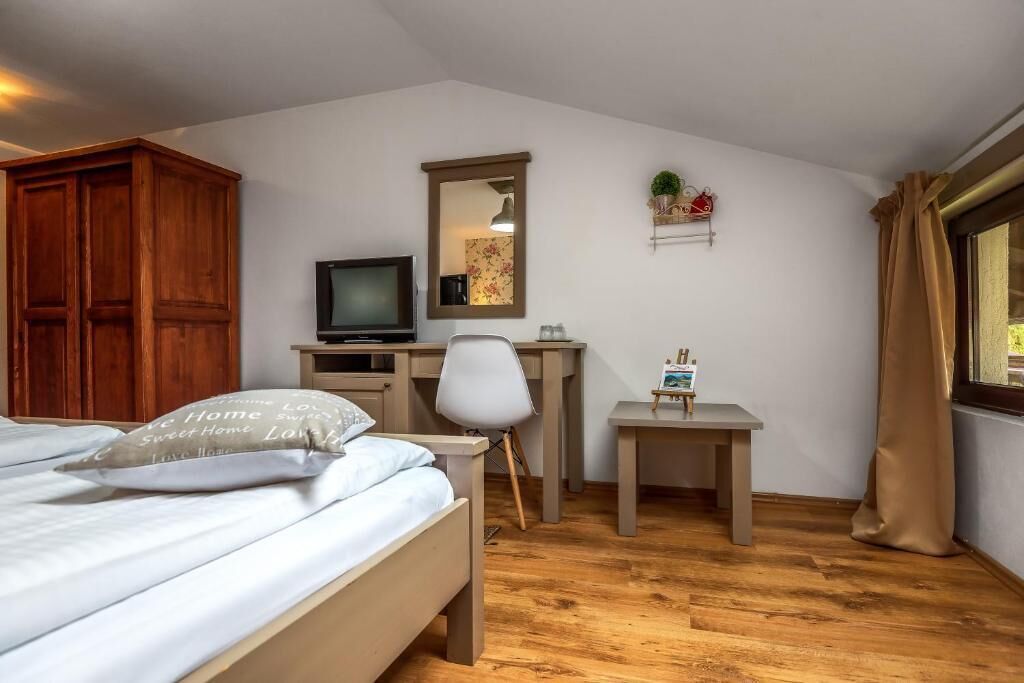 A bedroom with a bed, a desk, a chair, a TV, and a mirror.