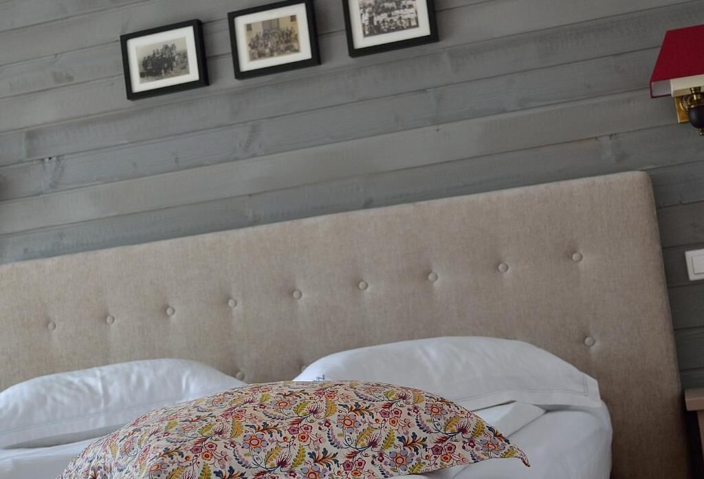 Quarto com cabeceira estofada, cama com roupa de cama branca e três quadros na parede.