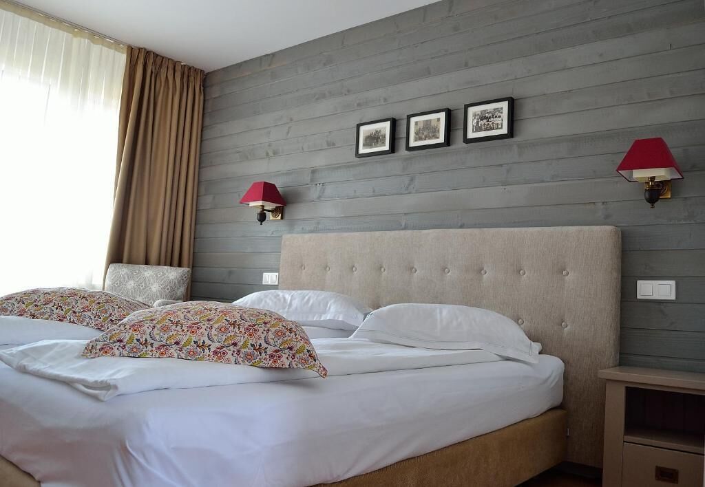Une chambre d’hôtel avec un grand lit, deux coussins décoratifs, une tête de lit, une table de chevet et des lampes fixées au mur.