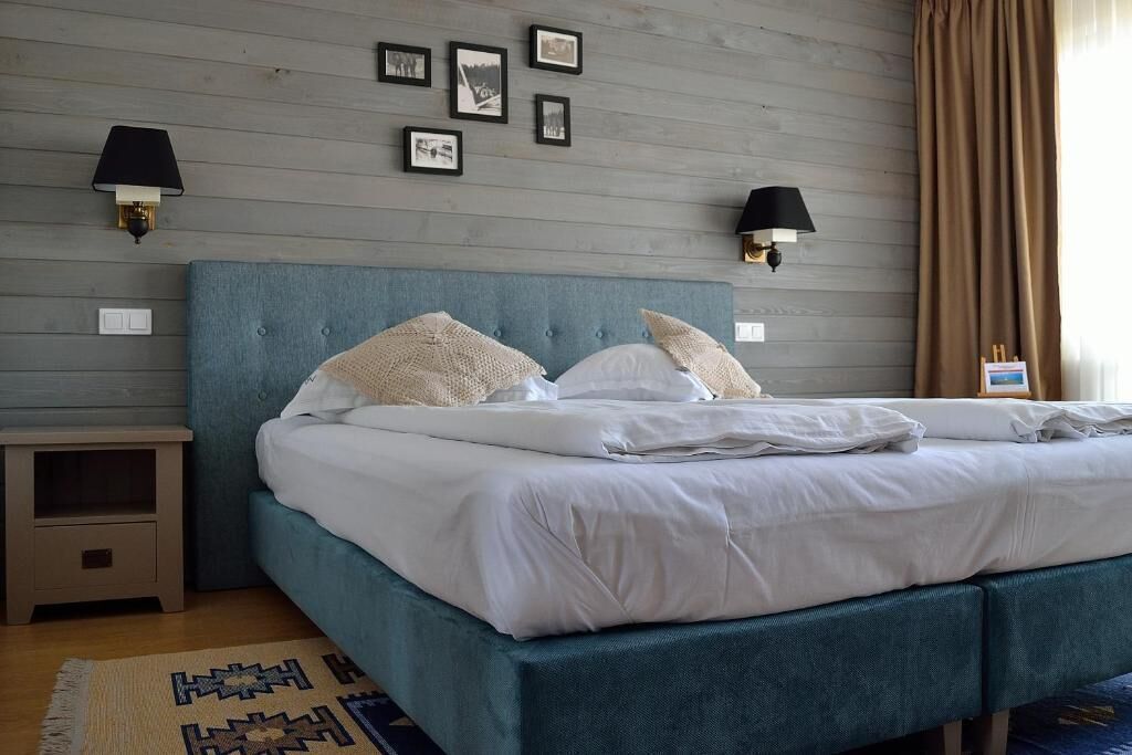 A neatly made bed with white linens, a teal upholstered headboard, and two wall-mounted lamps.