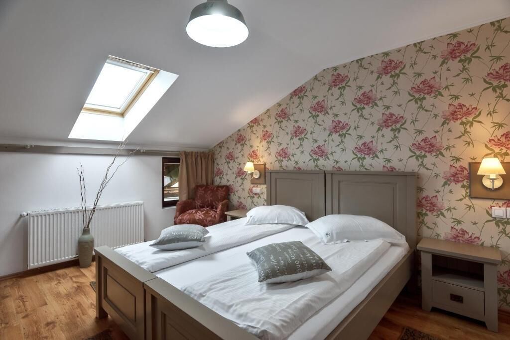 A bedroom with a skylight, floral wallpaper, a bed with pillows, a nightstand, and a radiator.