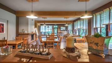 Un comedor amplio con mesas y sillas de madera, chimenea y ventanas grandes que dejan entrar luz natural.