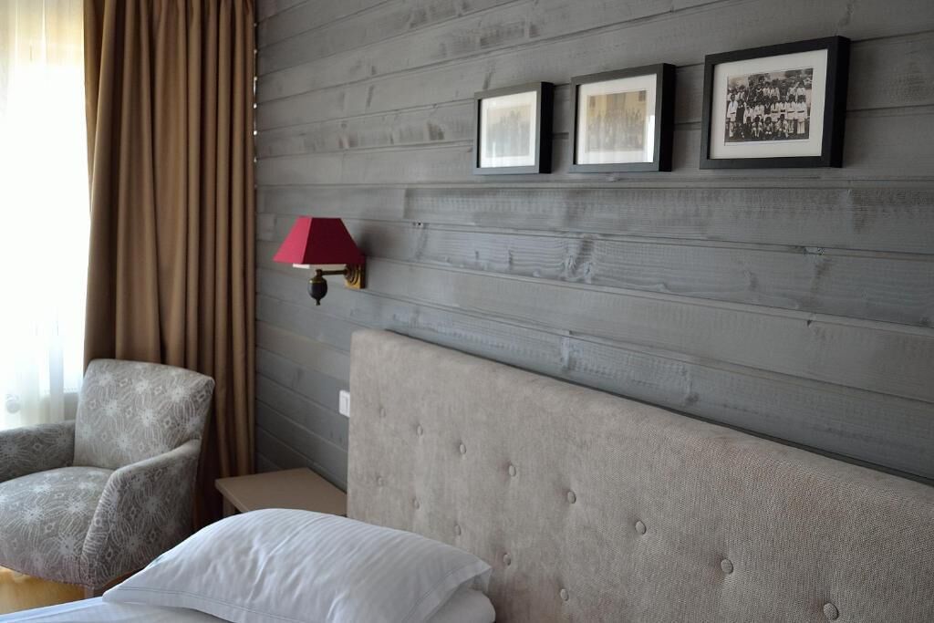 Ein Hotelzimmer mit grauem Kopfteil, einer roten Wandlampe, einem grauen Sessel und drei gerahmten Bildern an der Wand.