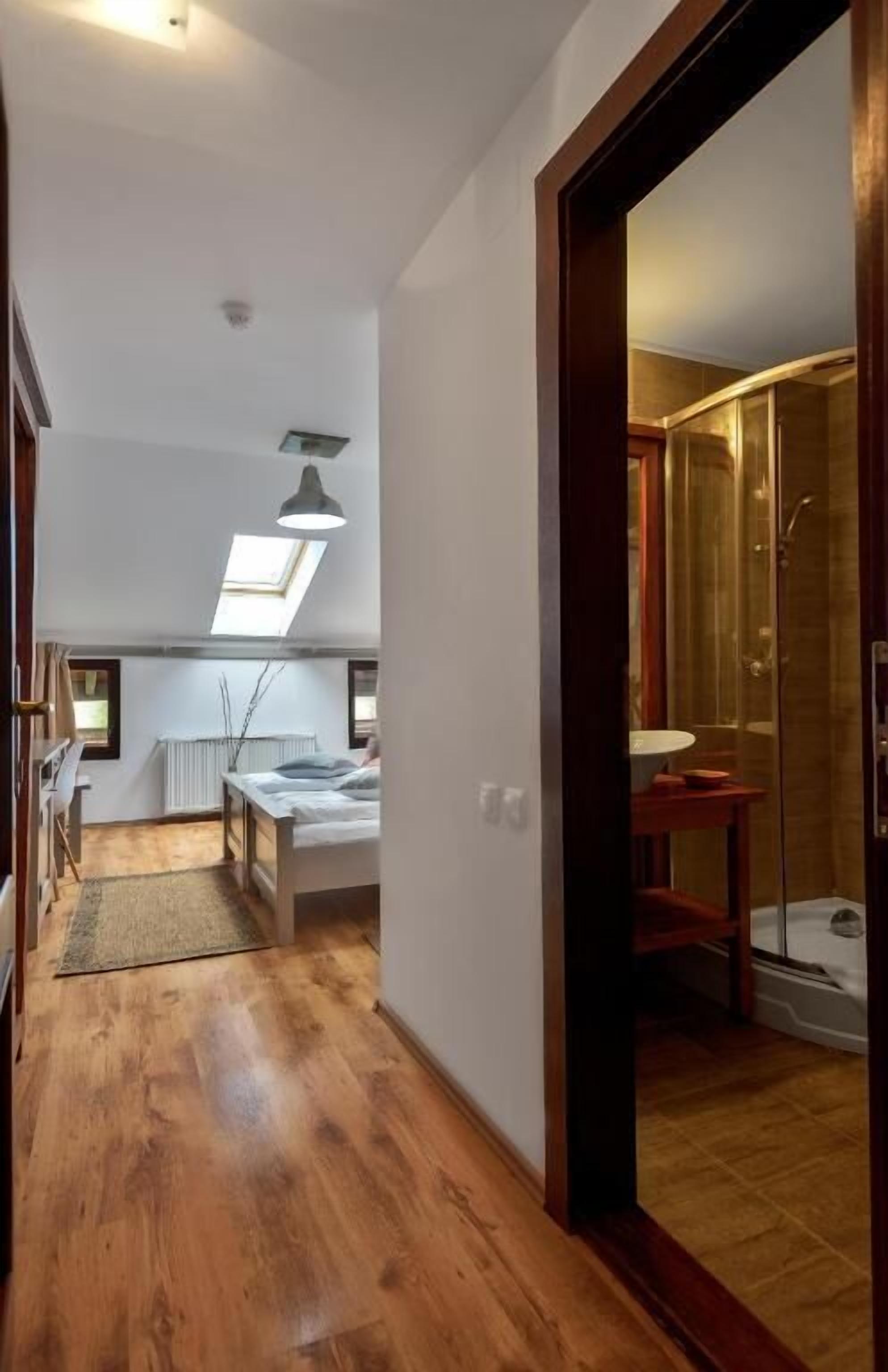 Un corridoio stretto conduce a una camera da letto con un lucernario, un piccolo angolo relax e un box doccia in vetro.