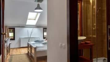 A narrow hallway leading to a bedroom with a skylight, a small sitting area, and a glass-enclosed shower.