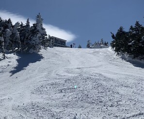 A snow-covered ski slope with a building in the background. - Cannon Mountain, NH. Slope side ski condo. 1 minute to Mittersill chairlift (Franconia)