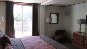 Quarto de hotel com uma cama grande, uma escrivaninha com luminária, uma cadeira, penteadeira e varanda com cortinas.