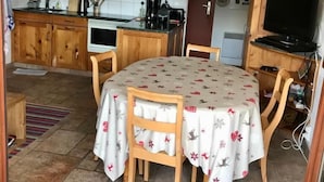 A compact kitchen with wooden cabinets, a dining table with floral tablecloths, and a television on a wooden stand.