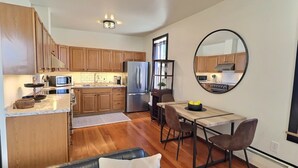 A modern kitchen with wooden cabinets, stainless steel appliances, and a dining area with a round mirror. - Fully-furnished Modern Apartment / Executive Suite in Heart of Town
 (Big Timber)