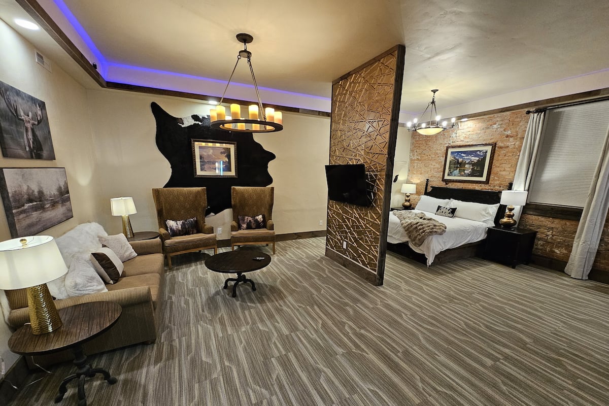 A hotel room with a seating area, a bed, a TV, and a decorative wall.