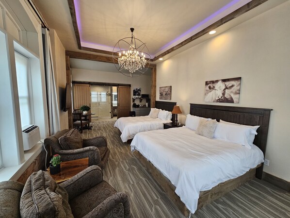 Une chambre d’hôtel avec deux lits, un lustre, un bureau avec une lampe, un canapé et une grande fenêtre.