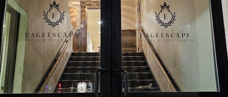 Un escalier menant à un bâtiment doté de portes en verre et d’un logo sur lequel on peut lire « EAGLESCAPE SUITES & EVENT CENTER ».