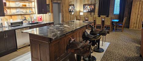 A kitchen with a large island, bar stools, wooden cabinets, and a patterned carpet.