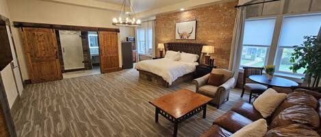 A spacious hotel room with a large bed, a wooden coffee table, a leather sofa, and a dining area with a table and chairs.
