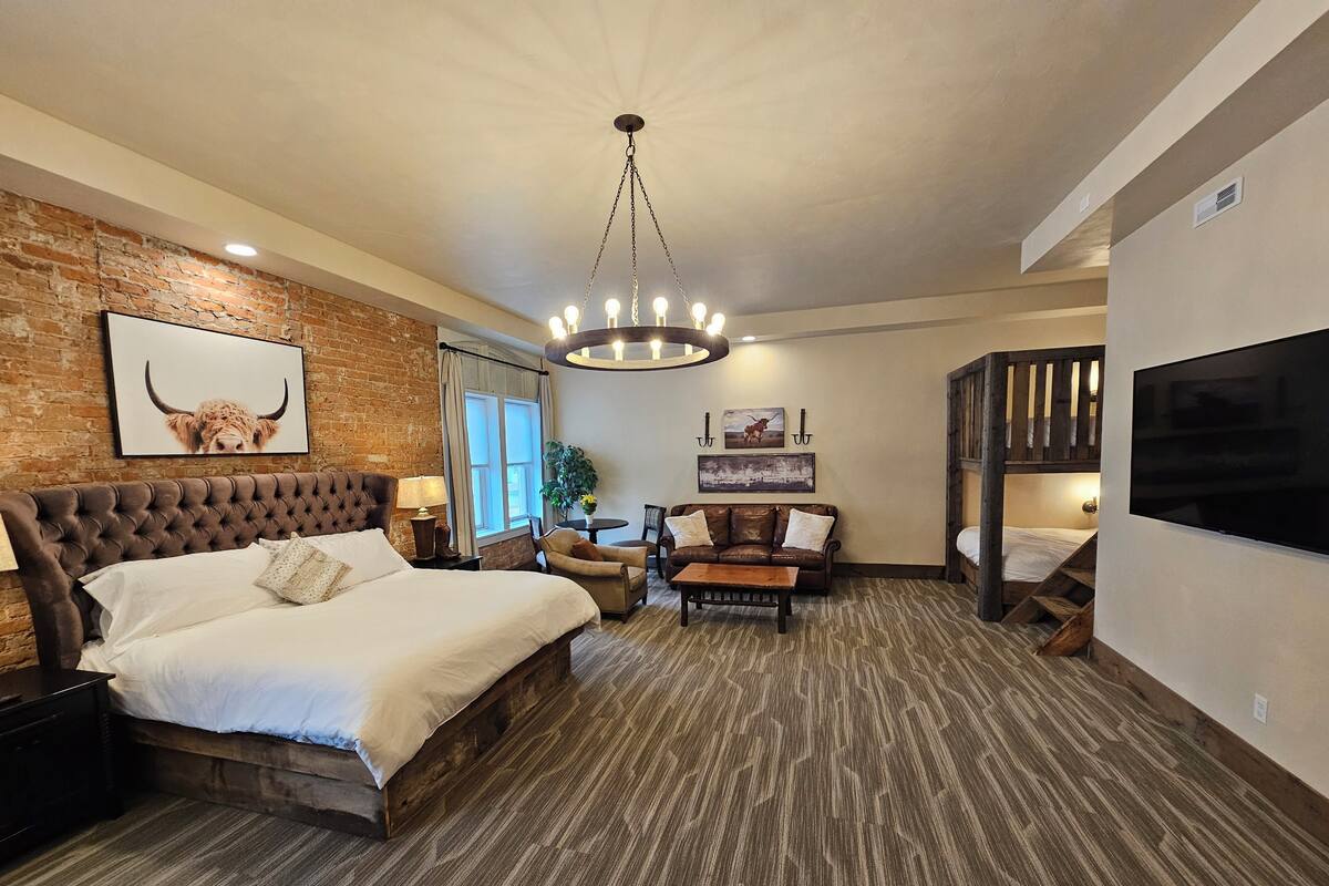 A bedroom with a large bed, a wooden headboard, a TV, a desk, and a staircase.