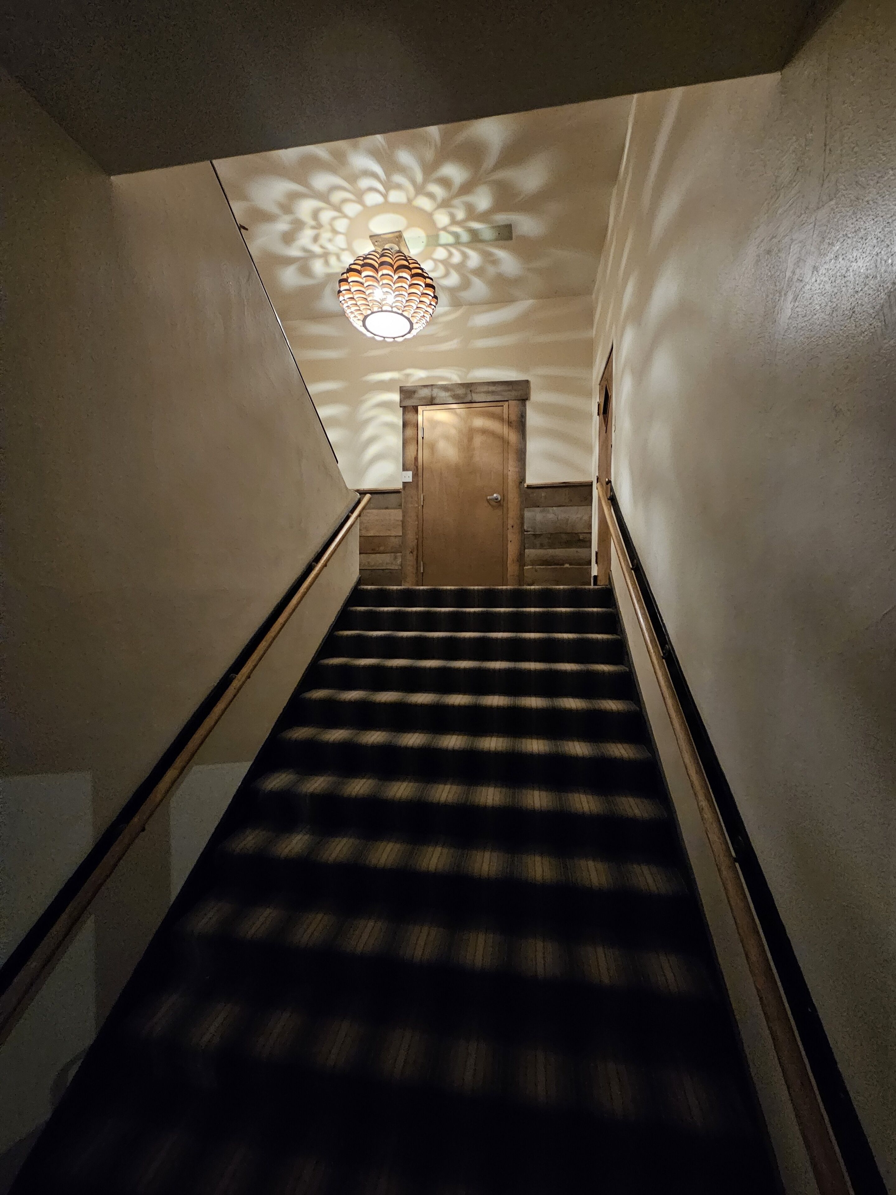 A staircase with a wooden door at the top, a patterned wall, and a decorative ceiling light.