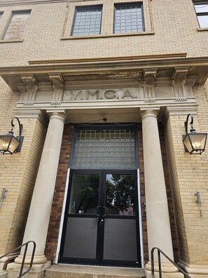 Une façade d’immeuble avec une grande entrée, des colonnes et l’inscription « Y.M.C.A. ».