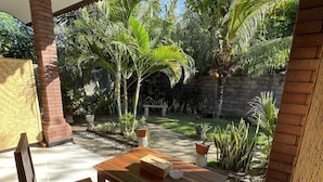 A patio with a wooden table and chairs, surrounded by a lush garden with various plants and a stone wall. - Tebu Menjangan (Pejarakan)