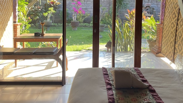 A room with a bed, a table, and a view of a garden through large glass doors. - Tebu Menjangan (Pejarakan)