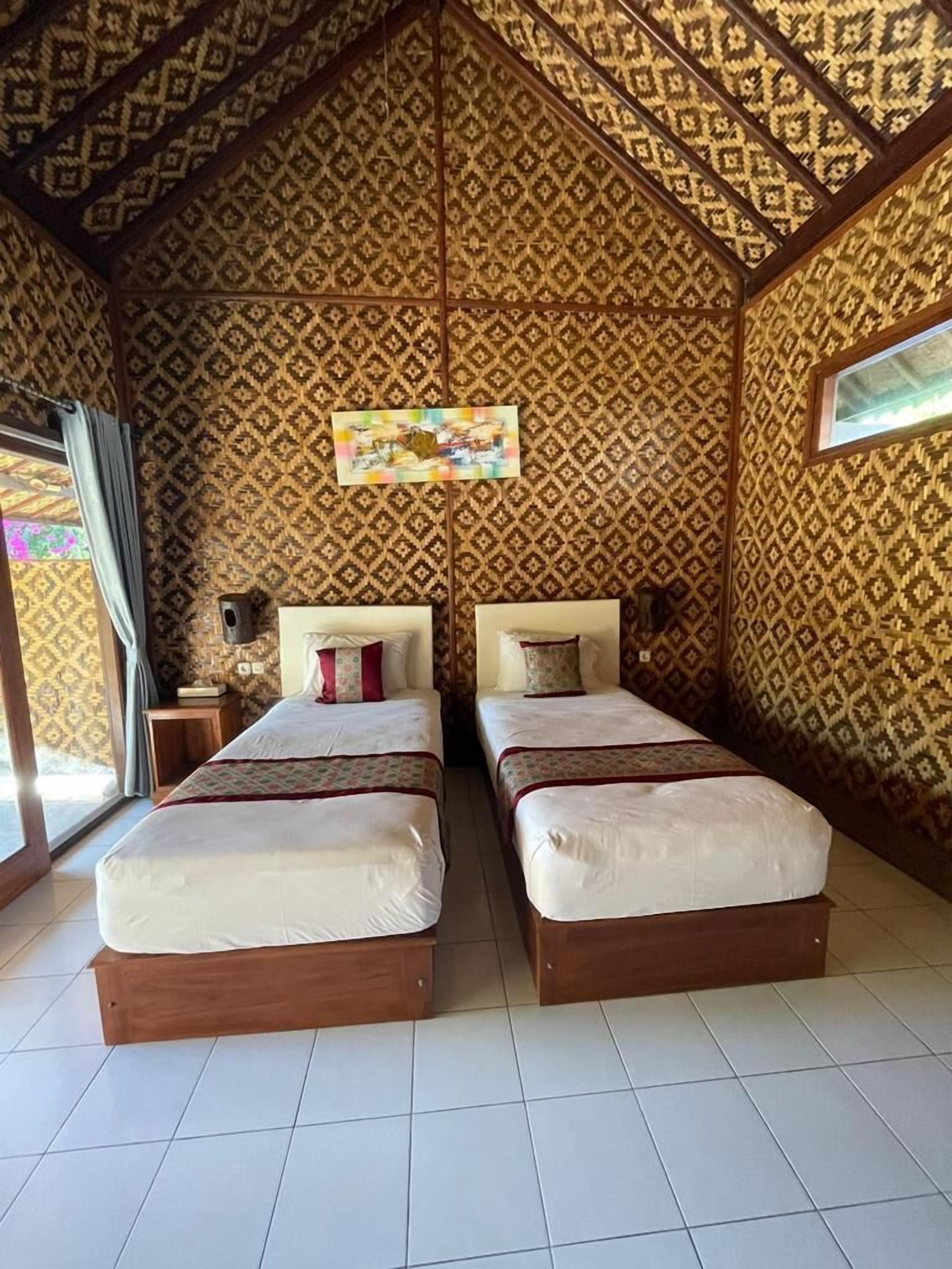 A room with two beds, patterned walls, a ceiling fan, and a window.