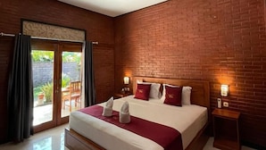 A hotel room with a large bed, a brick wall, a sliding glass door to a balcony, and a small bedside table with a lamp. - Tebu Menjangan (Pejarakan)