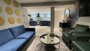 Een moderne woonkamer met een blauwe bank, een groene fauteuil en een ronde salontafel.