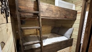 Llits superposats amb escala, parets de fusta i una petita estant.