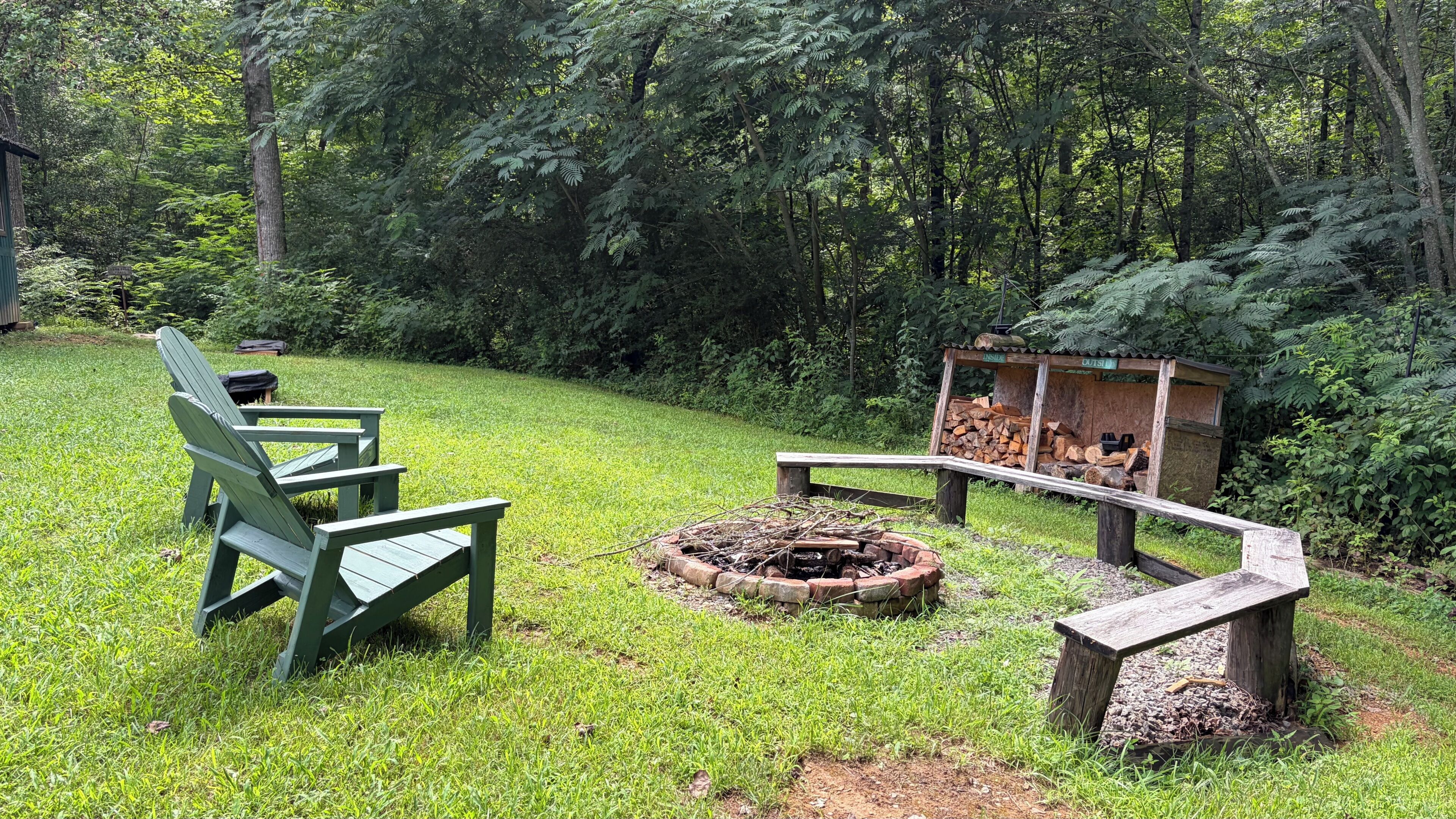 Un’area picnic con un braciere, panche e una piccola struttura in legno con tronchi.