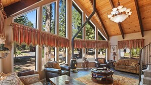 A spacious living area with large windows, a fireplace, leather furniture, and a wooden ceiling.