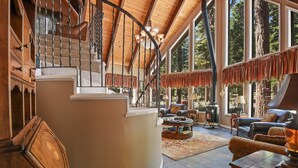 A spacious living area with a fireplace, leather furniture, and a large window overlooking a forested area. - 5-Bedroom Agate Bay Home, Lake & Skiing (Carnelian Bay)