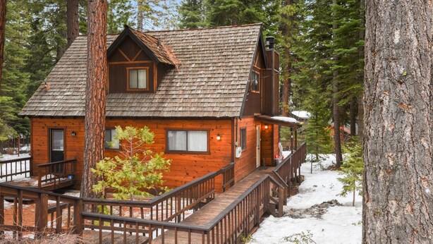Una cabaña de madera con un porche y una escalera, rodeada de árboles y nieve.