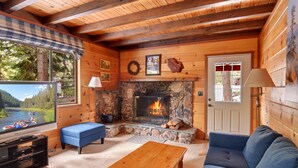Un interior de cabaña acogedor, con chimenea de piedra, paredes de madera, un televisor y un sofá.