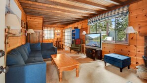 Interior acogedor de una cabaña de troncos con un sofá azul, una mesa de centro de madera y un televisor que muestra una escena de la naturaleza.