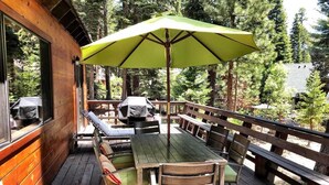 Un patio al aire libre con piso de madera, una mesa con sillas y una sombrilla verde.