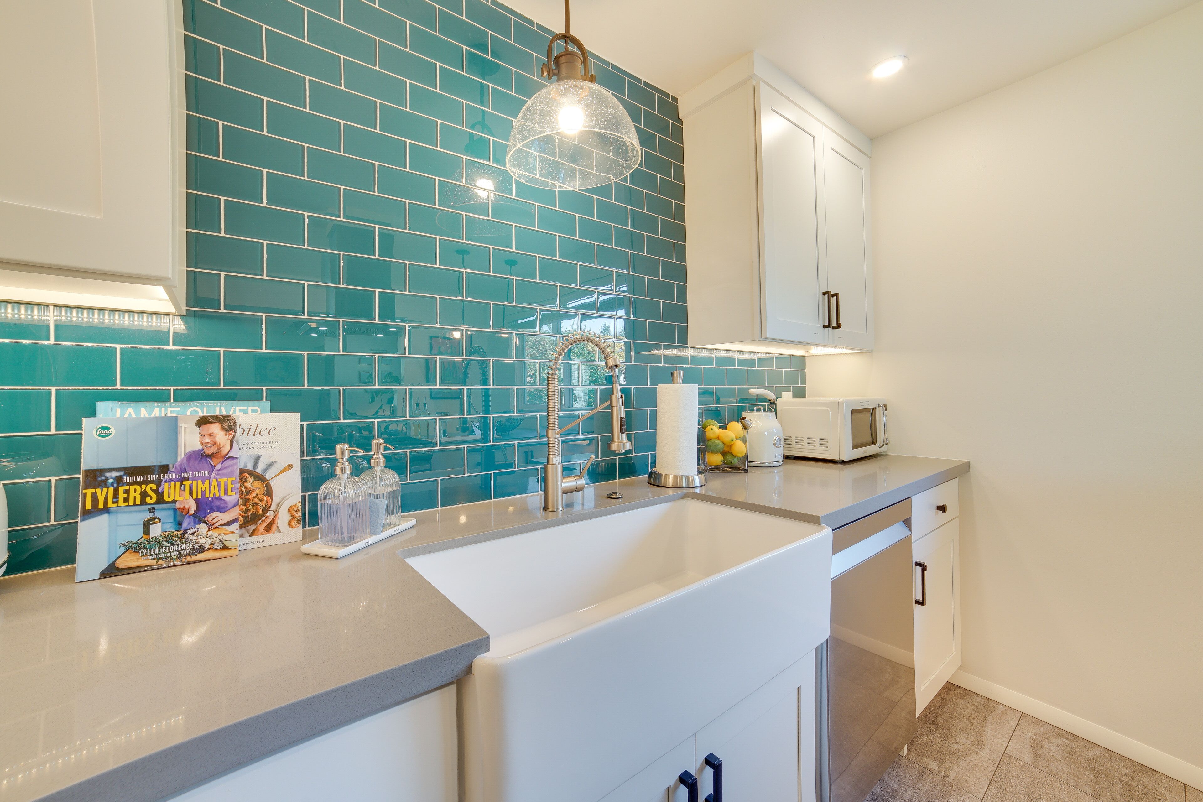 A modern kitchen with teal backsplash, white cabinets, and a stainless steel sink.