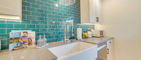 A modern kitchen with teal backsplash, white cabinets, and a stainless steel sink.