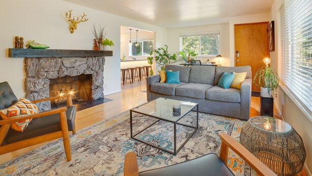 A living room with a stone fireplace, a sofa, a coffee table, and a dining area in the background. - Hot Tub, 5 Mi to Dtwn! Newly Updated Seattle Home (Seattle)