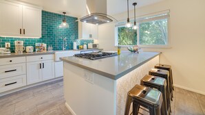A modern kitchen with white cabinets, a teal backsplash, a central island with stools, and a window providing natural light. - Hot Tub, 5 Mi to Dtwn! Newly Updated Seattle Home (Seattle)