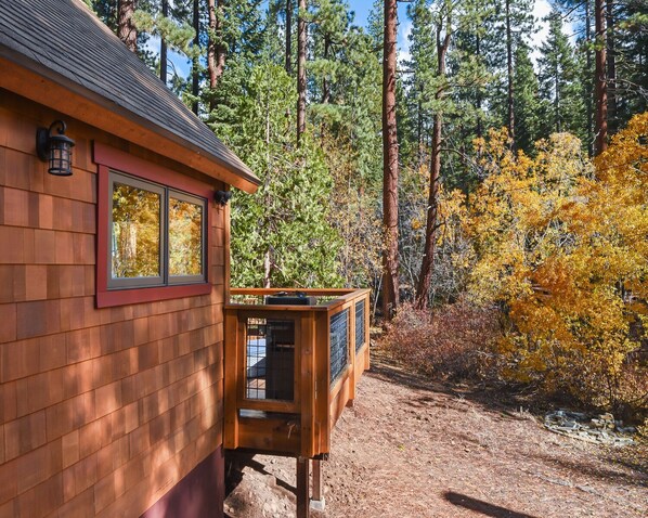 A wooden cabin with a window and a small wooden structure with a metal door, surrounded by trees and autumn foliage. - Lewis Lair - Renovated, Dog-Friendly, Lake & Ski (Tahoe Vista)
