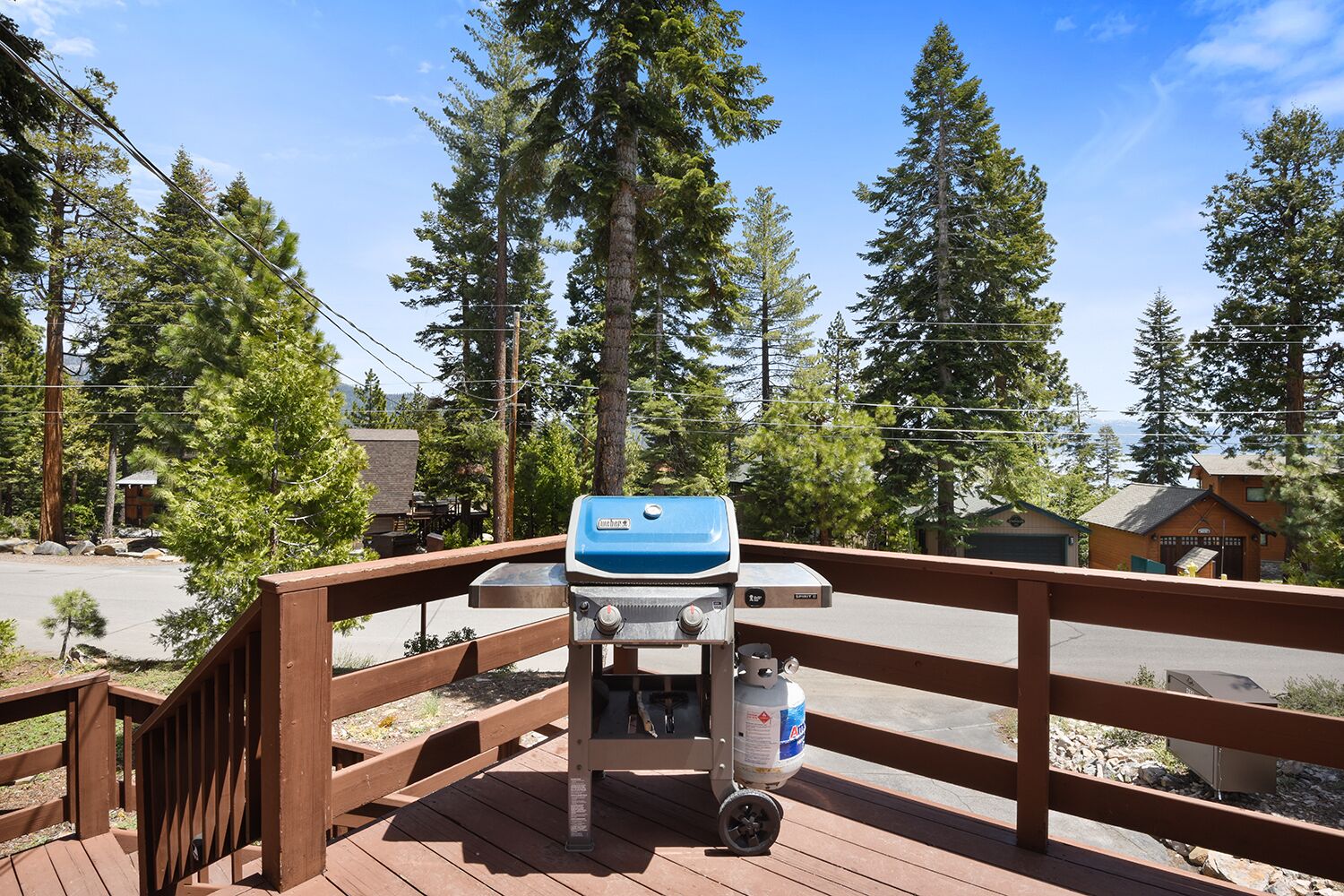 A barbecue grill on a wooden deck with a view of a forest and a building in the background.