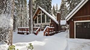 A log cabin with a large deck and a garage, surrounded by snow-covered trees.